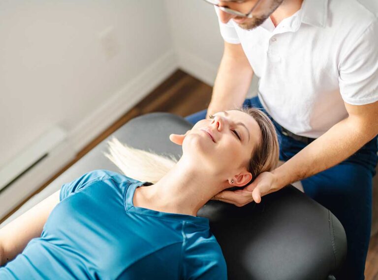 A chiropractor demonstrating gentle stretching techniques with an older adult in a home setting.