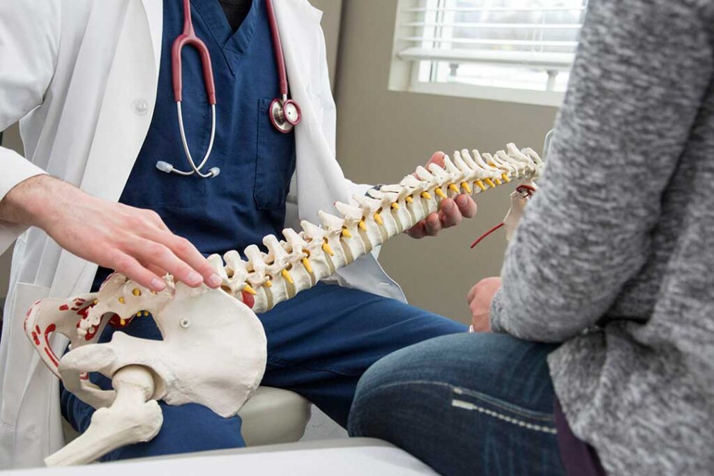 Adult doing guided back mobility exercises beside a treatment table in a bright wellness room.
